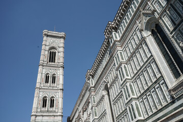 A tall building of Florence Cathedral with a clock tower and a blue sky in the background
