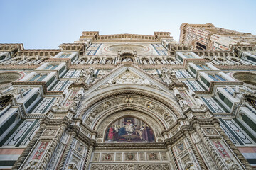 A tall building of Florence Cathedral with a clock tower and a blue sky in the background