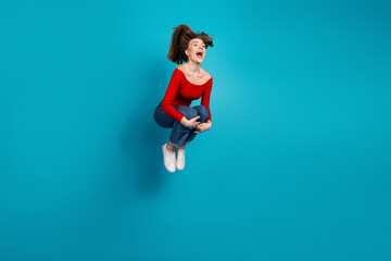Joyful woman in a vibrant red top and blue jeans joyfully jumping on a bright blue background, full...