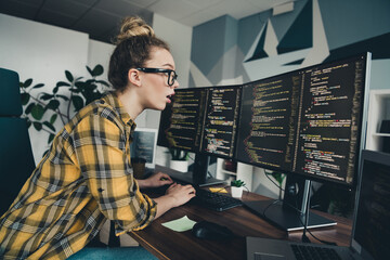 Young female programmer coding on dual monitors in a modern workspace emphasizing software...