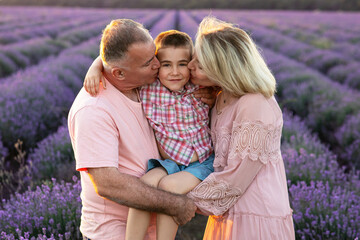 Beautiful friendly family: dad, mom and their son in purple lavender field at sunset in summer