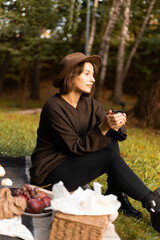 A cozy autumn moment as a woman drinks tea on a picnic near a still lake, embraced by nature’s rich fall colors.