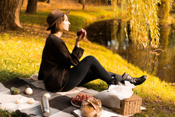 A woman bites into a fresh apple during an autumn picnic near a calm lake, surrounded by cozy textures and nature.