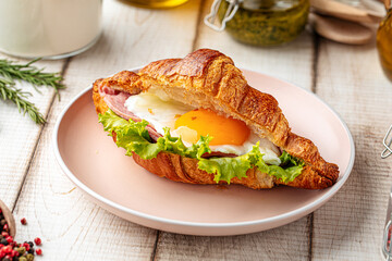 Croissant sandwich with fried egg, ham and lettuce on breakfast table