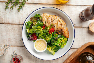 Healthy lunch bowl with grilled chicken, fresh salad and broccoli on rustic wooden table