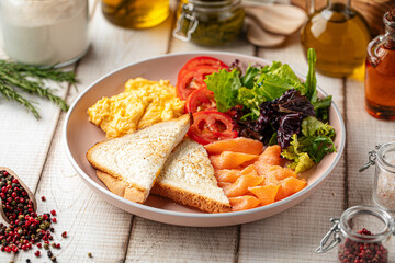 Healthy breakfast plate with scrambled eggs, toast, smoked salmon and fresh vegetables