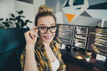 Qualified female programmer smiling confidently while coding at her modern workspace with dual...