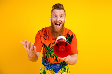Cheerful young man in tropical t-shirt holding a red megaphone, expressing joy against a vibrant...