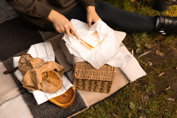 Woman’s hands spreading butter on a slice of bread at an outdoor autumn picnic with a woven...