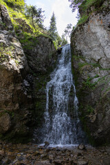 Waterfall cascading down mossy rocks in Kok Zhailau, Kazakhstan, surrounded by green cliffs