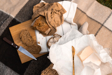 A rustic picnic setup with fresh bread, butter, and a knife laid out on a checkered blanket in...