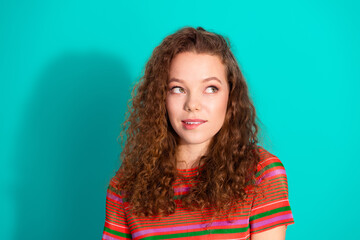 Charming young woman with curly hair wearing a colorful striped t-shirt standing against turquoise...