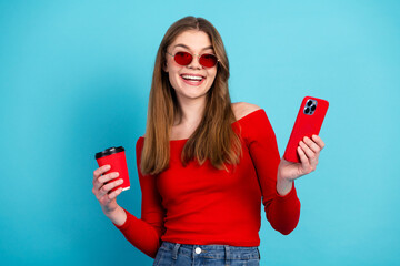 Happy young woman with a smartphone and coffee cup, wearing red and looking stylish against a blue...