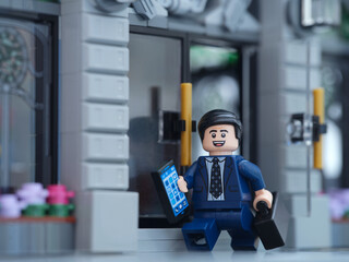 Obraz premium Tambov, Russian Federation - July 06, 2025 A happy Lego businessman minifigure walking out of a bank and holding a cell phone and a briefcase.