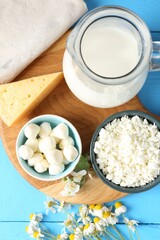 Different fresh dairy products and flowers on light blue wooden table, flat lay