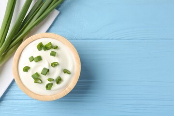 Tasty yoghurt with green onions in bowl on light blue wooden table, flat lay. Space for text