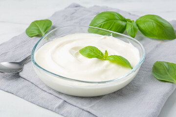 Tasty yoghurt with basil in bowl on white table, closeup
