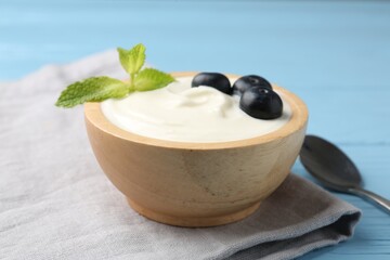 Tasty yoghurt with blueberries and mint in bowl on light blue wooden table, closeup