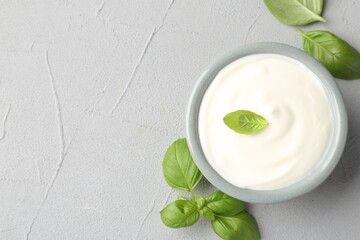 Tasty yoghurt with basil in bowl on light grey table, flat lay. Space for text