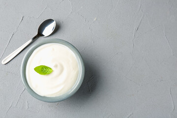 Tasty yoghurt with basil in bowl on light grey table, top view. Space for text