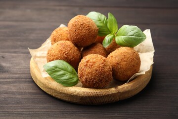 Delicious fried croquette balls with basil on wooden table, closeup