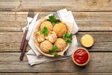 Delicious fried croquette balls with parsley and sauces served on wooden table, flat lay