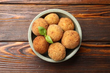 Delicious fried croquette balls with basil in bowl on wooden table, top view
