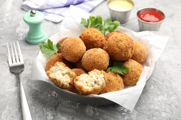 Delicious fried croquette balls with parsley in bowl and fork on grey textured table, closeup