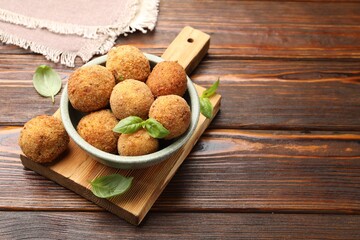 Delicious fried croquette balls with basil in bowl on wooden table, closeup