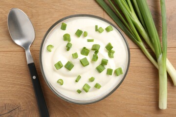 Delicious yogurt in bowl, green onions and spoon on wooden table, flat lay
