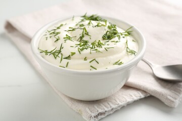 Delicious yogurt in bowl and dill on white marble table, closeup