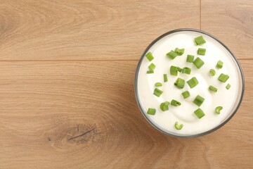 Delicious yogurt with green onions in bowl on wooden table, top view. Space for text