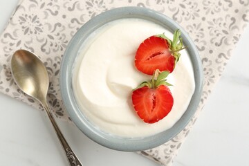 Delicious yogurt in bowl, strawberries and spoon on white table, flat lay