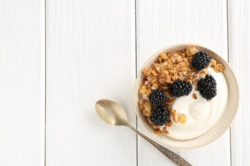 Tasty yogurt with granola and blackberries in bowl on white wooden table, top view. Space for text