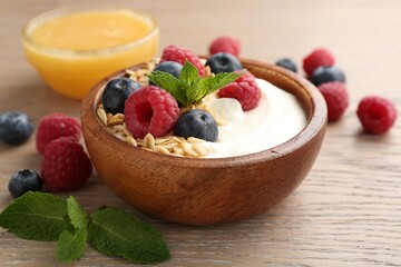 Tasty yogurt with granola, honey and berries in bowl on wooden table, closeup