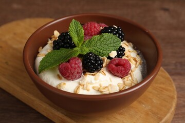 Tasty yogurt with granola and berries in bowl on wooden table, closeup