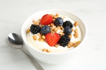 Tasty yogurt with granola and berries in bowl on white marble table, closeup