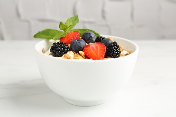 Tasty yogurt with granola and berries in bowl on white marble table, closeup