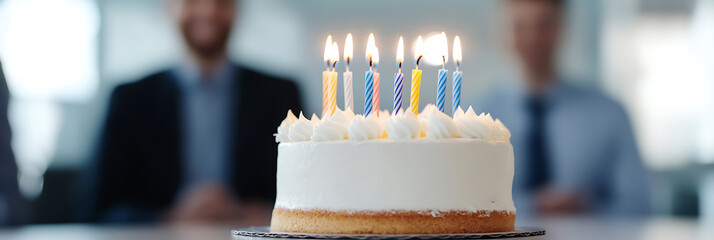 Celebratory moment with a birthday cake adorned with lit candles, shared in an office environment with colleagues.