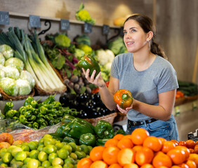 Joyful young woman chooses green and red bell peppers