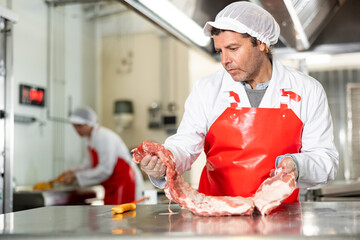 Male kitchen worker closely examines raw meat for cutting and preparing for sale