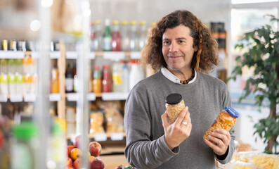 Adult man buyer chooses beans in jar in grocery store
