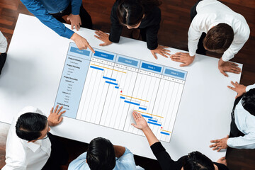 A diverse business team gathers around a table, discussing project management strategies displayed...
