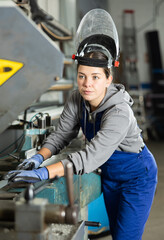 Girl employee wearing safety face shield performs hazardous work in production. She is close to...