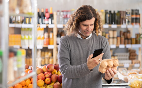 Customer in a European store holds a package of eggs in his hands and scans a barcode on a mobile phone. Man uses an online application to pay by QR code
