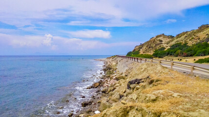 Coastal road winding along the Aegean Sea with rocky cliffs and calm blue waters. Captured on the island of Rhodes on a clear summer day.