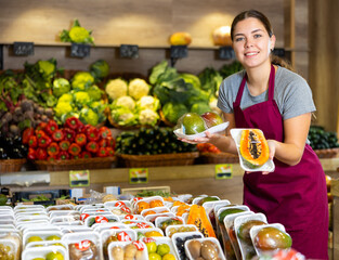 Female grocery store worker offers various packaged fruits and vegetables