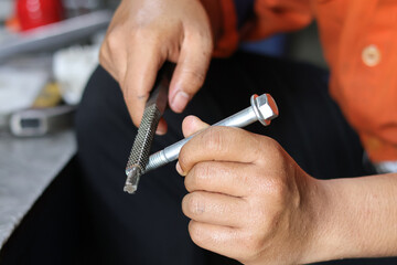Fototapeta premium Close up of a hand cleaning a bolt thread using a thread file. Industrial concept.
