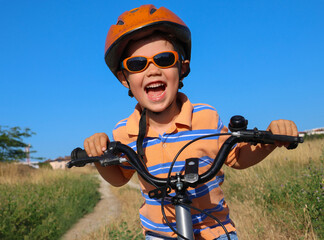 small brave three year old boy in a helmet rides a bicycle on a field road by himself