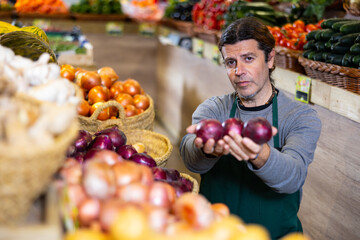 Male grocery store worker arranges red onion and other vegetables on the counter and display case